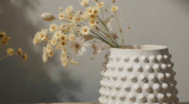 Ahşap zemin üzerinde çiçek olan beyaz seramik kap.