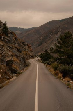 Arkasında kayalık dağlar olan dağlık bir arazinin ortasında dolambaçlı bir yol.