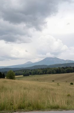 Arkasında bulutlu bir gökyüzü olan bir dağ manzarası.