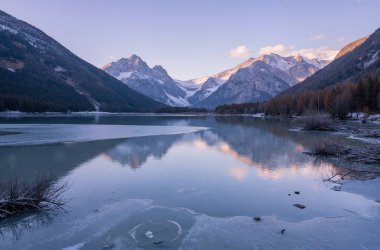 Uzakta karla kaplı dağlarla çevrili donmuş bir göl. Ön planda buz oluşumları var.