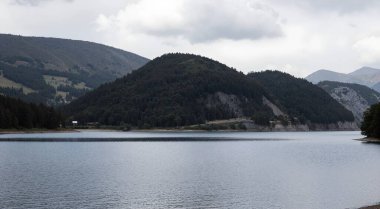 Bulutlu gökyüzünün altında dağlarla çevrili büyük bir su kütlesi.