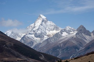 Açık mavi gökyüzünün altında karla kaplı tepeleri olan bir dağ sırası.