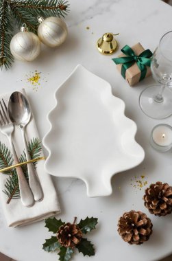 Köknar ağacı, çatal bıçak takımı ve tabakla Noel sofrası.