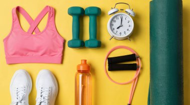 Ölçüm bandı ve sarı arkaplandaki dambıllar ile fitness minderinin üst görünümü