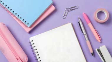 Pembe ve beyaz renkli kalemler ve pembe arka planda not defteri..