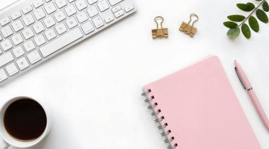 Bilgisayar, defter, kahve ve bitkinin beyaz ahşap arka planda olduğu düz bir çalışma alanı.