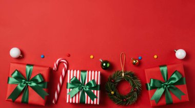 Kırmızı arka planda noel ağacı süslemeleri, hediye kutuları, kırmızı kurdele ve yeşil yaprakların düz kompozisyonu. Yeni yıl kutlamaları.