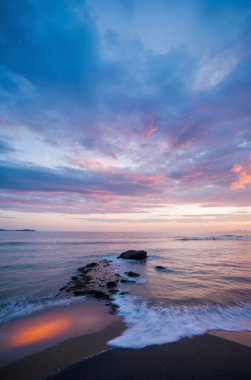 Okyanusun üzerinde renkli bir günbatımı kayalık bir kıyı şeridi ve kumlara vuran dalgalarla