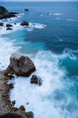 A rocky coastline with waves crashing against the rocks and pebbles, creating a beautiful contrast between the deep blue water and the rocky shoreline