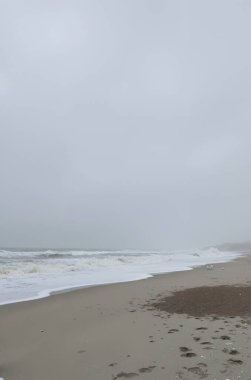 Bulutlu bir arka planda büyük dalgaları olan güzel bir sahil manzarası.