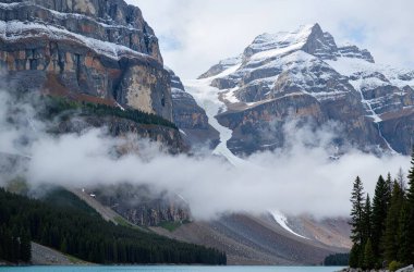 Kanada 'da bulutlu gökyüzünün altında dağlarla çevrili güzel bir göl görüntüsü.