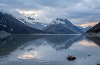 Bulutlu bir kayağın altında dağlarla çevrili büyük bir su kütlesi.