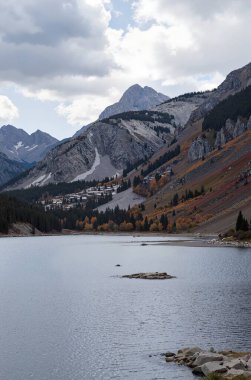 Gündüz vakti bulutlu gökyüzünün altında dağlarla ve yeşilliklerle çevrili güzel bir göl görüntüsü.