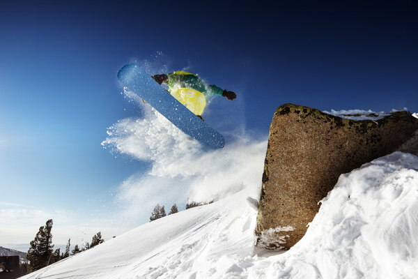 Snowboarder jumps from big rock