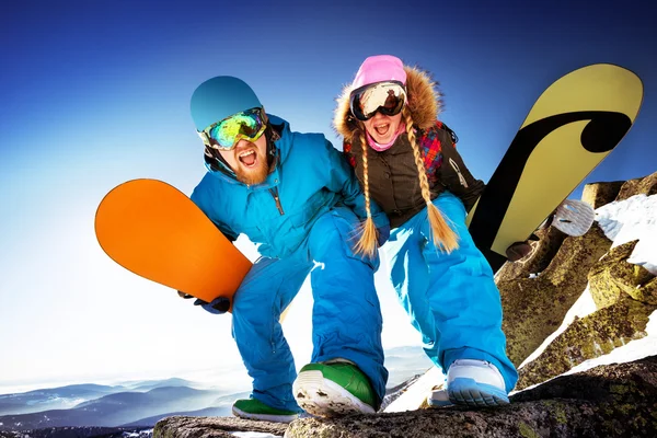 Una pareja feliz de snowboarders está parada en una roca grande. Fondo de las montañas — Foto de Stock