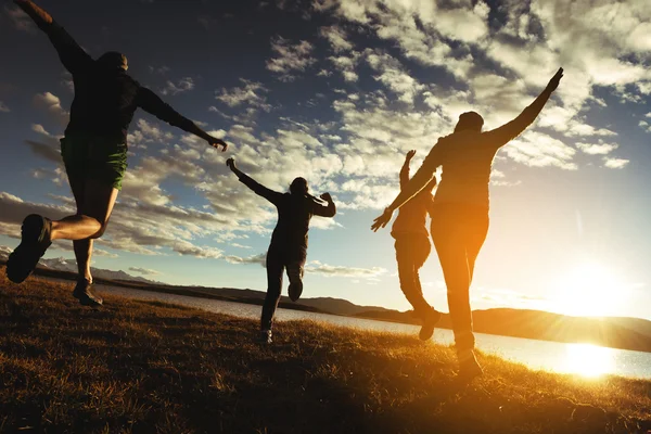 Grupo de amigos corre a la puesta de sol lago y montañas — Foto de Stock