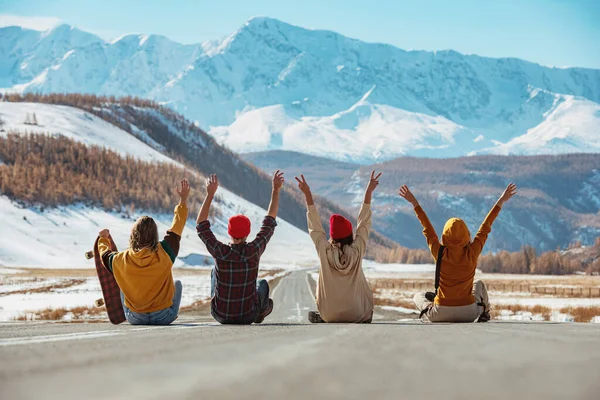 Vier gelukkige vrienden met opgeheven armen zit op rechte bergen weg — Stockfoto