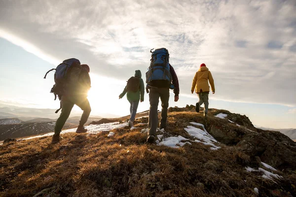 Caminhantes com mochilas caminham nas montanhas ao pôr do sol — Fotografia de Stock