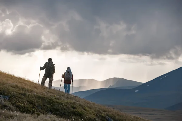 Dois caminhantes estão na encosta da montanha contra o pôr do sol — Fotografia de Stock