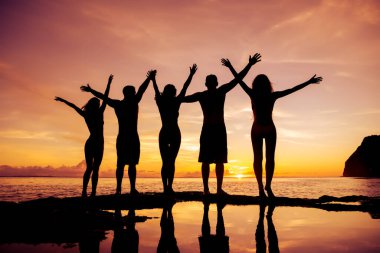 Beş mutlu arkadaş günbatımı denizinde kollarını kaldırmış bekliyor.