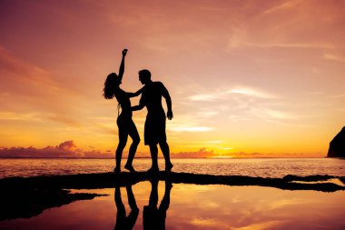 Romantik çift gün batımında deniz sahilinde sarılıyor.