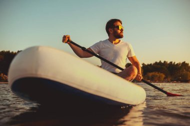 Hippi adam günbatımında kürek tahtasında oturur.