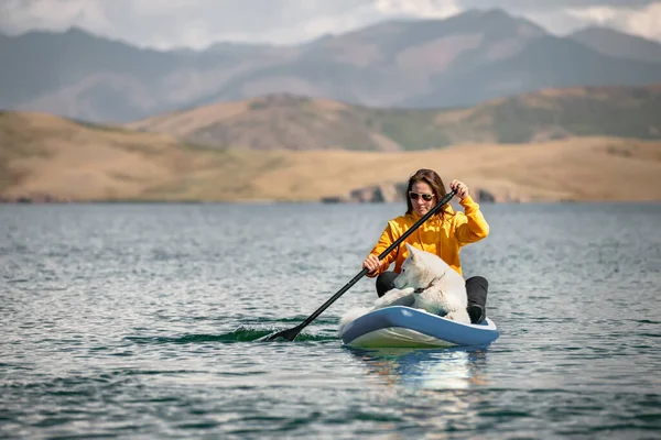 Menina caminha em prancha de jantar no lago da montanha com cão — Fotografia de Stock