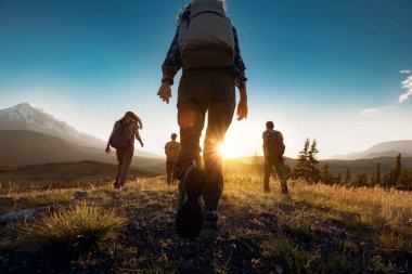 Bir grup sportif insan gün batımında sırt çantalarıyla dağlarda yürüyor.