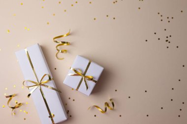 Altın kurdeleli beyaz hediye kutuları, altın renkli konfeti ile serpiştirilmiş bej arka plan manzarası