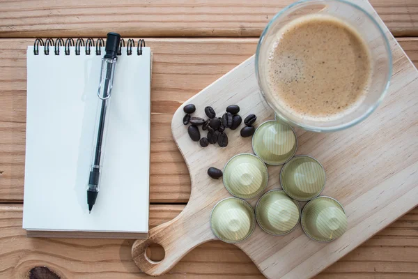 Café expreso y cápsula con granos de café sobre mesa de madera . — Foto de Stock