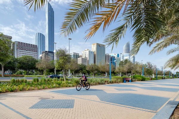 АБУ-ДАБИ, ОАЭ - 30 апреля 2021 года: Человек на велосипеде по Абу-Даби Corniche утром с современным городским пейзажем на заднем плане. Активный образ жизни. — стоковое фото
