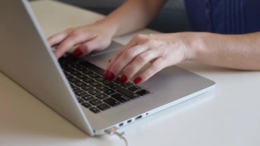Kırmızı ojeli bir kadın dizüstü bilgisayarda yazı yazıyor. Ellerini odakla. Evden bağımsız çalışma kavramı.