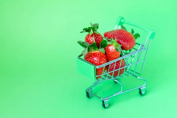 Frische leckere Erdbeeren im Einkaufswagen auf pastellgrünem Hintergrund, Einkaufskonzept — Stockfoto