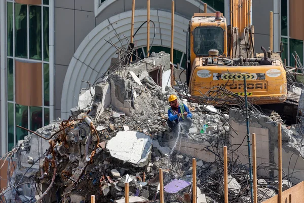 Abu Dabi, BAE - 22 Mayıs 2021: Su hortumlu adam beton parçalarını soğutuyor yıkım kazıcısı tarafından tahrip edildi