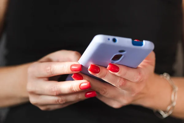 Cep telefonu kullanan bir kadın, ellerinde kırmızı oje manikürlü eller. İnternetten alışveriş.