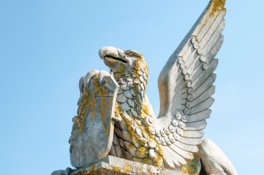 Bir kalkan tutan bir kaide üzerinde kanatlı bir efsanevi yaratık heykeli