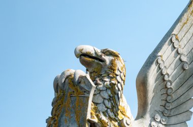 Bir kalkan tutan bir kaide üzerinde kanatlı bir efsanevi yaratık heykeli