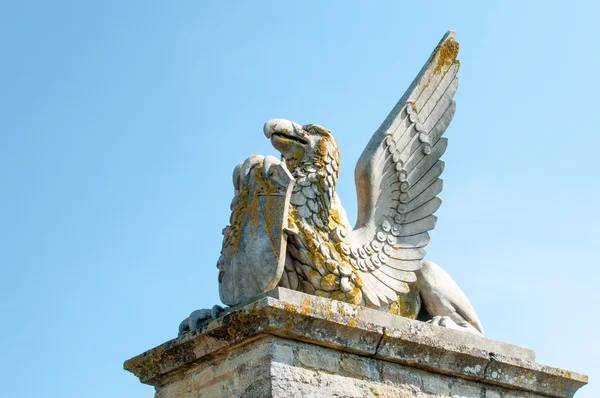 Bir kalkan tutan bir kaide üzerinde kanatlı bir efsanevi yaratık heykeli