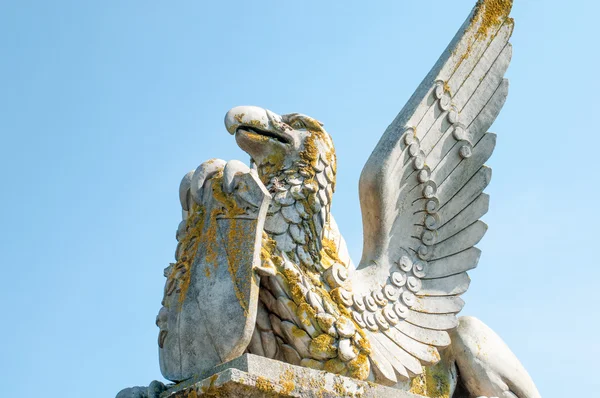 Bir kalkan tutan bir kaide üzerinde kanatlı bir efsanevi yaratık heykeli