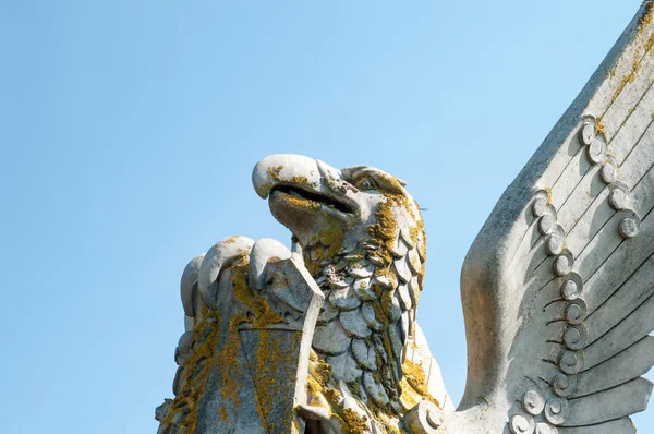 Bir kalkan tutan bir kaide üzerinde kanatlı bir efsanevi yaratık heykeli