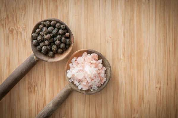 Salt and pepper seasonings of pepper corns and rock salt on wood