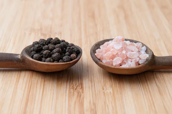 Salt and pepper seasonings of pepper corns and rock salt on wooden spoons