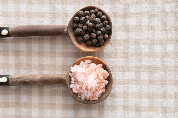 Salt and pepper seasonings of pepper corns and rock salt on wooden spoons