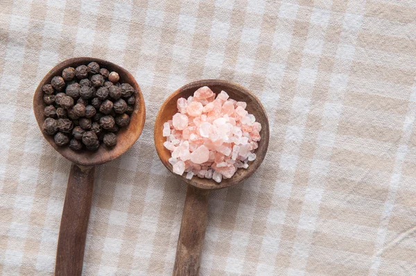 Salt and pepper seasonings of pepper corns and rock salt on wooden spoons