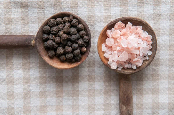 Salt and pepper seasonings of pepper corns and rock salt on wooden spoons