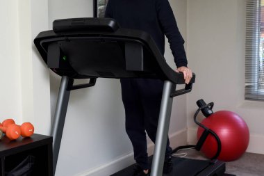 Evdeki spor salonundaki koşu bandında koşan bir adam.
