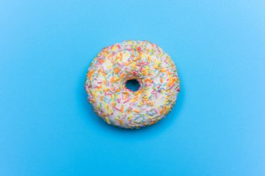 Mavi arka planda beyaz kremalı ve renkli parçacıklarla kaplanmış buzlu donut.