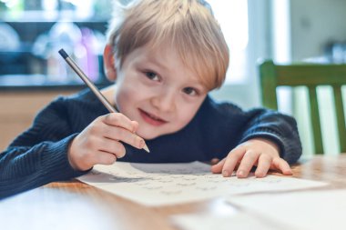 Çocuk ev hapsi sırasında mutfak masasında ödev yapıyor.