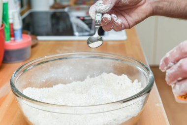 Ev mutfağında ekmek yapan kişi hamur yapmak için malzeme ekliyor.