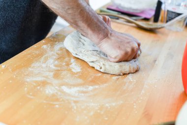 Ev mutfağında ekmek yapan kişi hamur yapmak için malzeme ekleyip elle yoğuruyor.